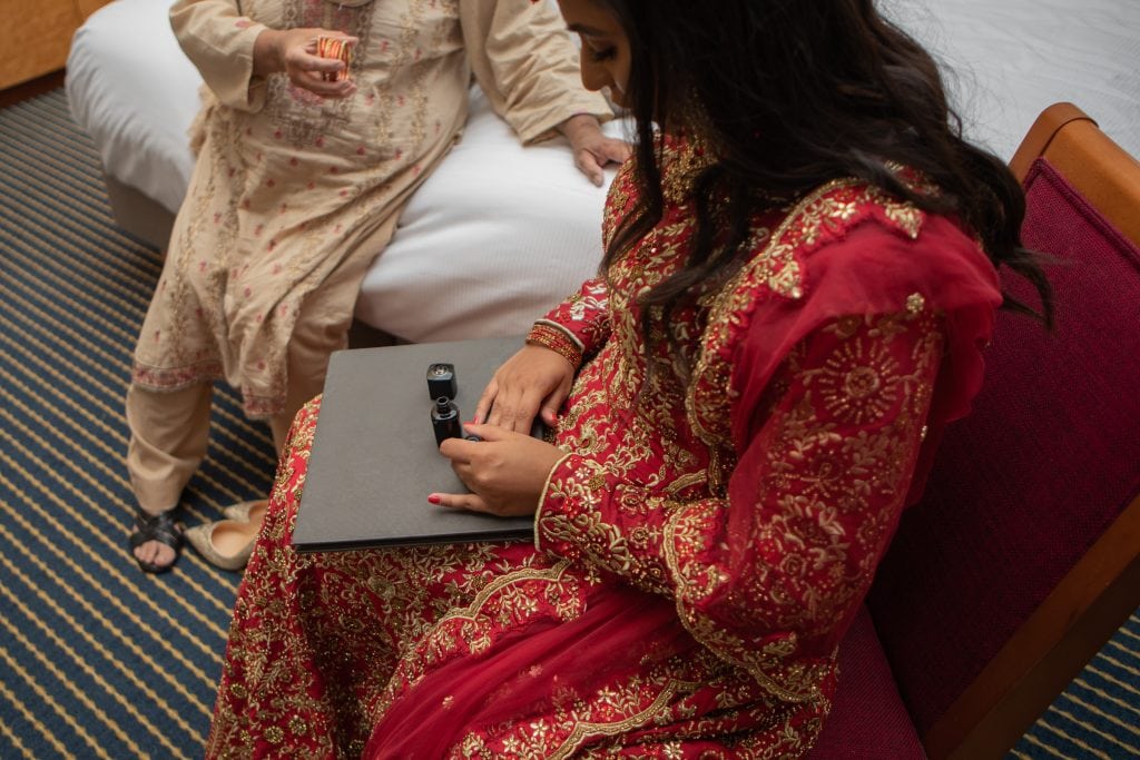 bride painting her nails red with channel nail varnish.